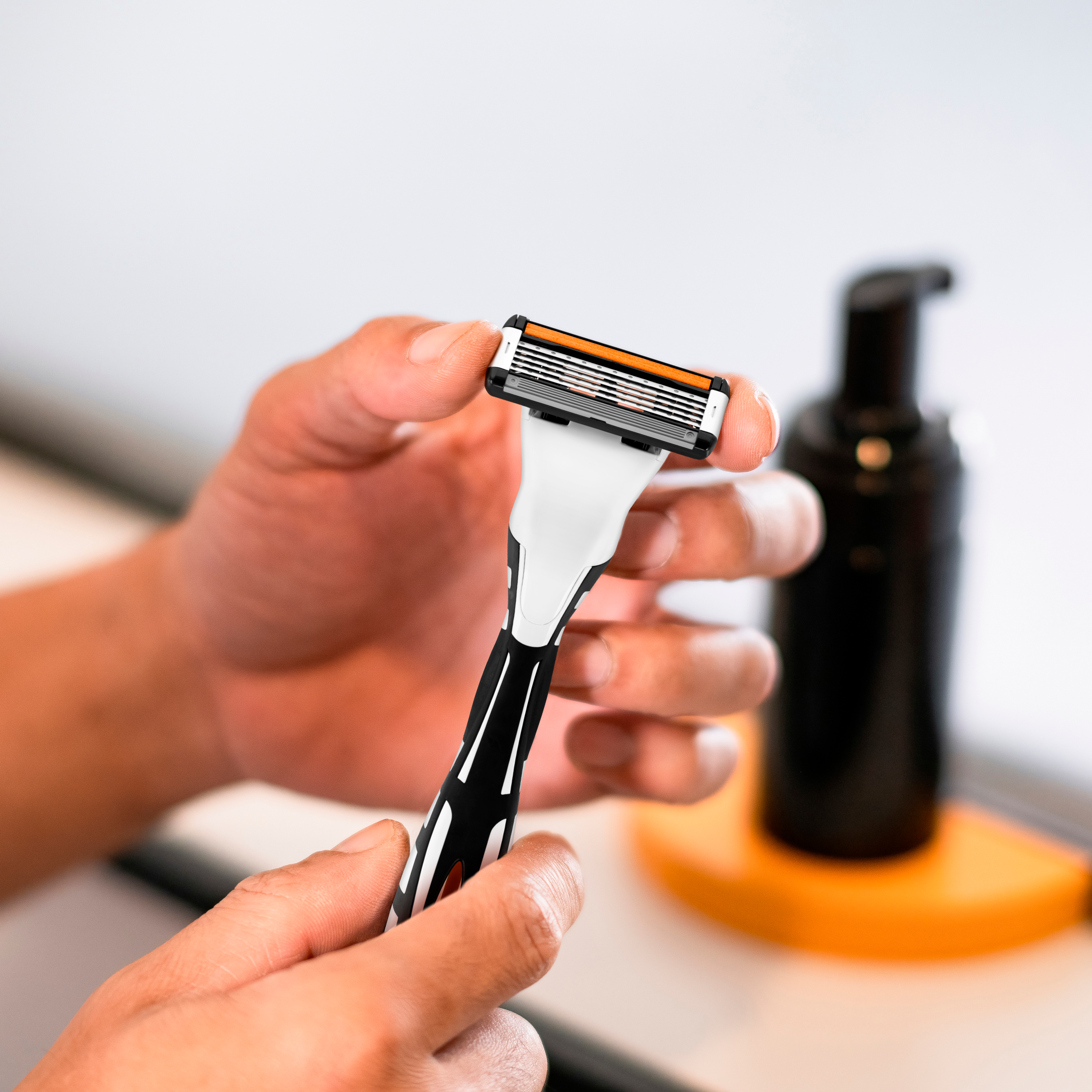 H&auml;nder h&aring;ller en rakhyvel i badrumsmilj&ouml;.