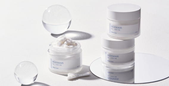 Tv&aring; burkar med Mixsoon hudkr&auml;m staplade ovanp&aring; varandra och en &ouml;ppen burk med kr&auml;m p&aring; en spegelplatta. Runt produkterna finns dekorativa genomskinliga sf&auml;rer.