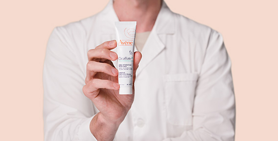 En person i vit laboratorierock h&aring;ller upp en tub Av&egrave;ne Cicalfate+ kr&auml;m.